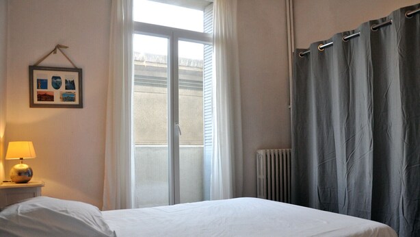Une chambre d’hôtel avec un lit, une table de chevet avec une lampe, une fenêtre avec des rideaux et un radiateur.