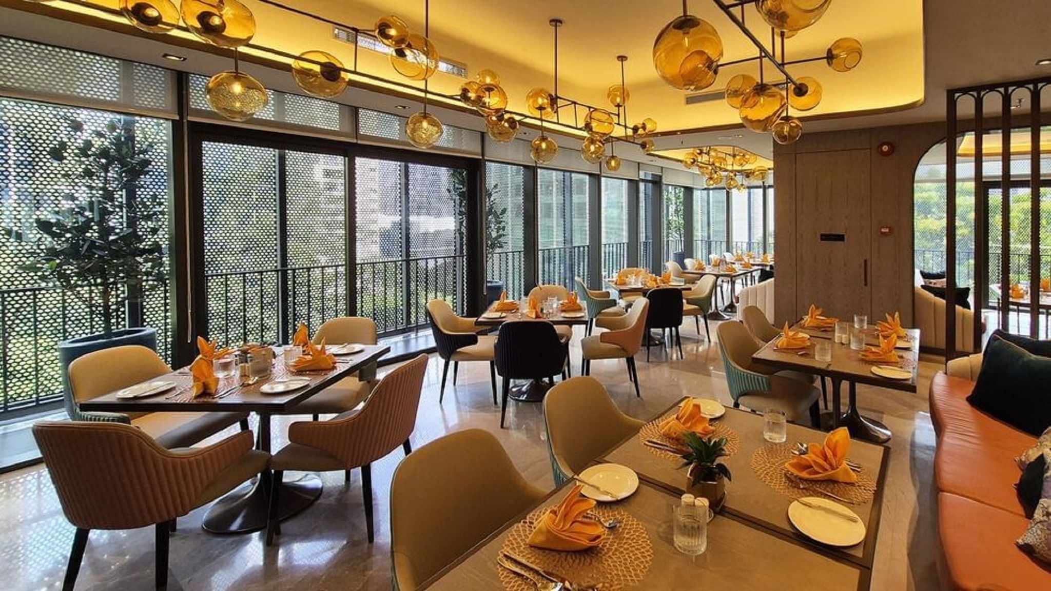 A modern dining area with multiple tables and chairs, large windows, and a decorative ceiling light fixture.