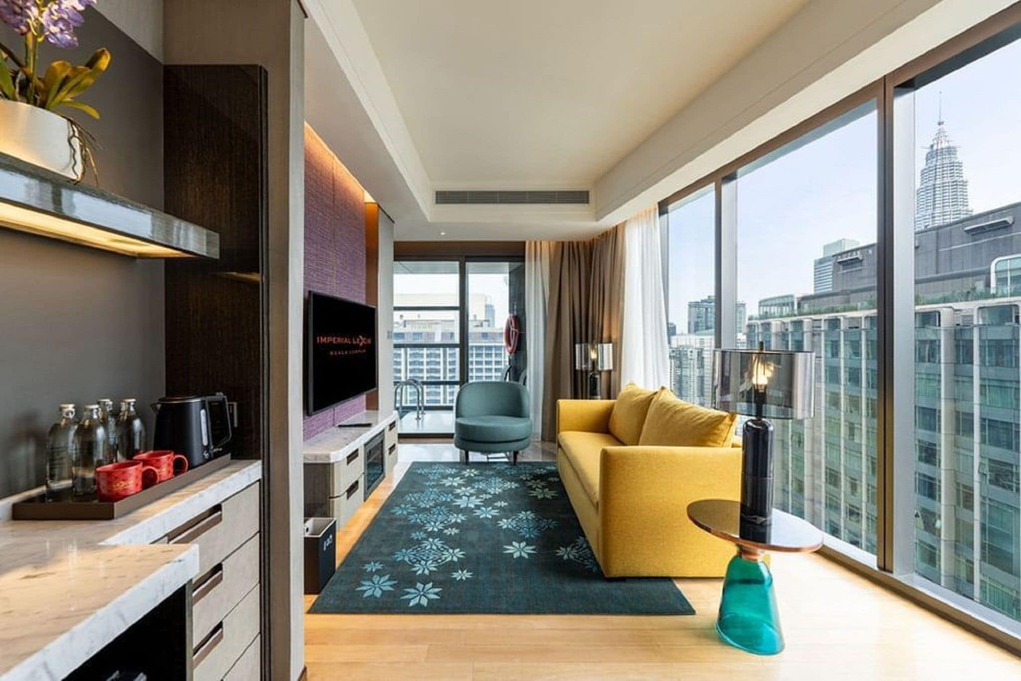 Een moderne woonkamer met een bank, een salontafel en een televisie. Er is een groot raam met uitzicht op de stad.
