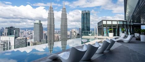 Een dakterras met een glazen overloopzwembad, modern zitmeubilair en uitzicht op de Petronas Towers.
