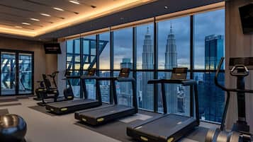 A modern gym with treadmills, stationary bikes, and a large window overlooking a cityscape.