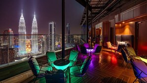 Un salón en la azotea con vistas a la ciudad, que cuenta con una mesa grande y sillas, además de una zona de bar.