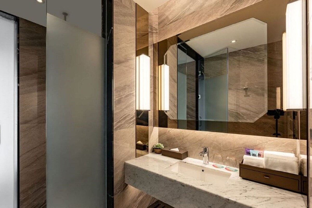 A modern bathroom with a marble countertop, a large mirror, and a glass shower enclosure.