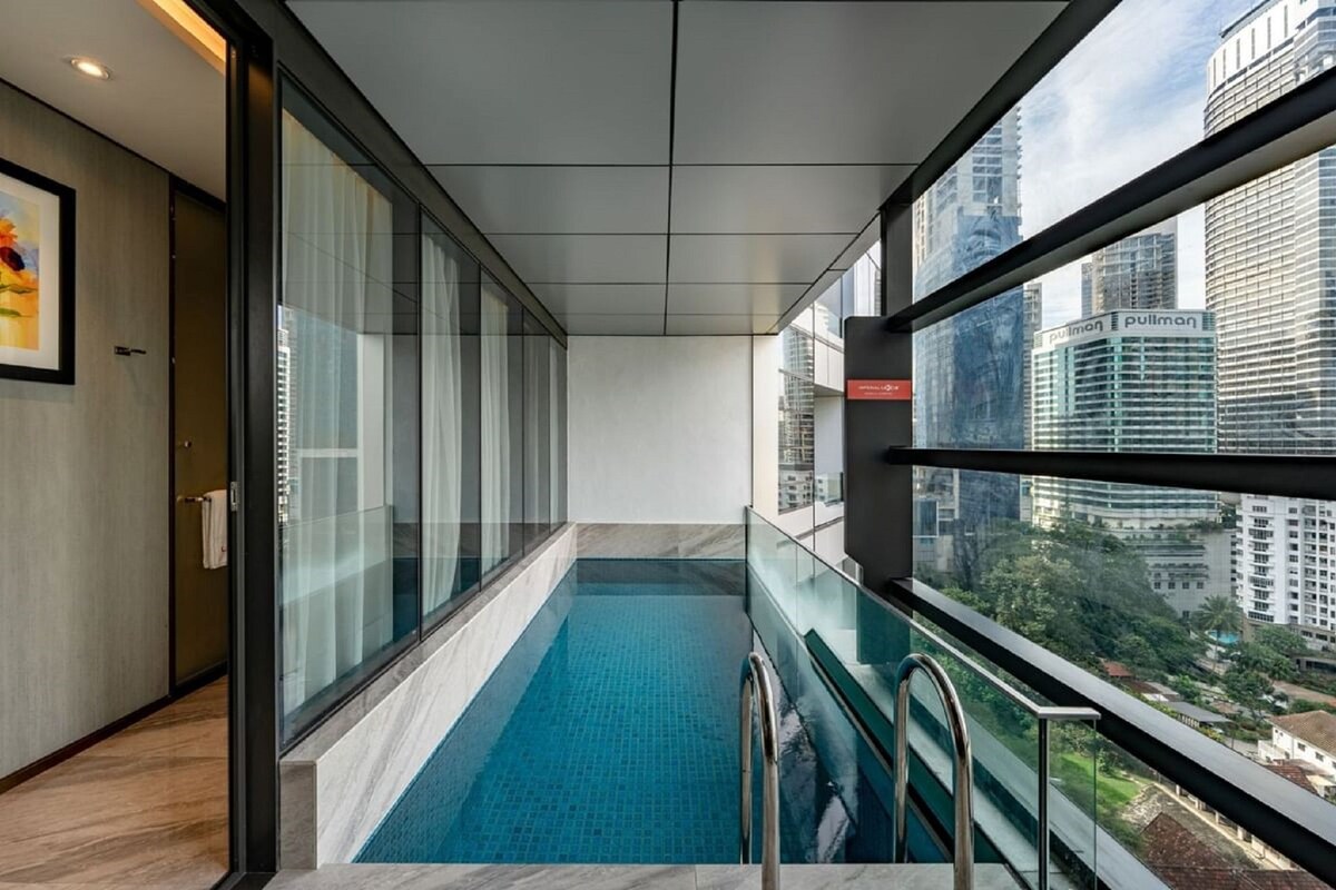 A modern hotel room with a glass-enclosed pool, city views, and a minimalist design.