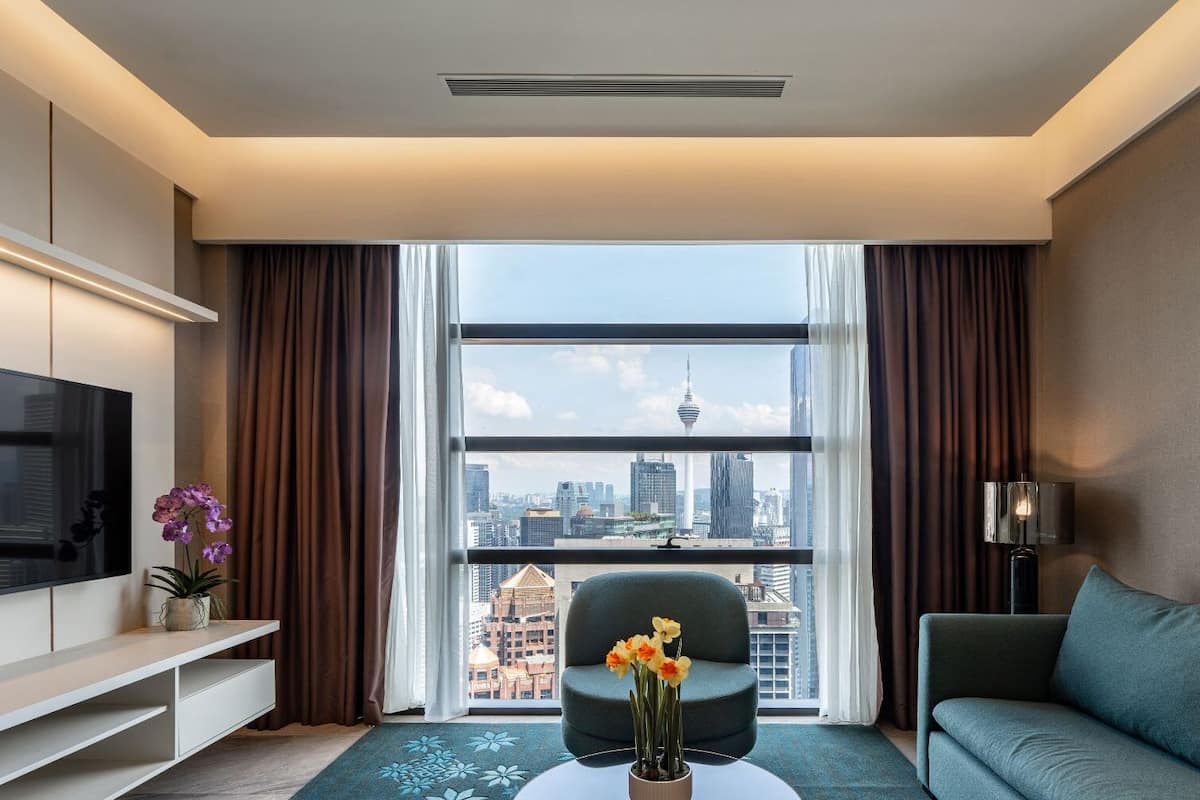 Een moderne hotelkamer met een groot raam met uitzicht over de stad, een flatscreen-tv, een bank en een kleine tafel met bloemen.
