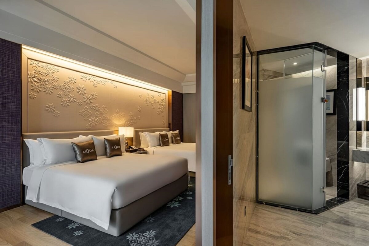 A hotel room with a large bed, a separate bed, a glass shower enclosure, and a decorative wall panel.