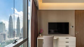 A modern hotel room with a large window, a flat-screen TV, a small desk, and a wardrobe.