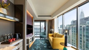 Una sala de estar moderna con un sofá, una mesa de centro y un televisor. Se observa un amplio ventanal con vistas a la ciudad.