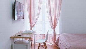 Une chambre à coucher avec un lit, un bureau et une chaise, un téléviseur et une fenêtre avec des rideaux légers.
