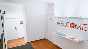 Un couloir avec une pancarte « BIENVENUE », une indication pour le dépôt de bagages et une étagère remplie de brochures.