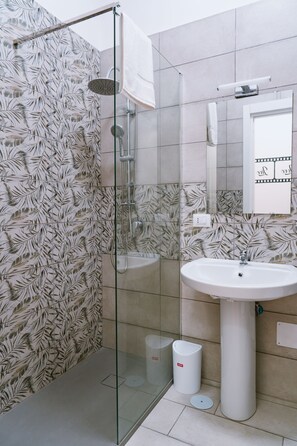 Een moderne badkamer met een douchecabine van glas, een witte wasbak en een spiegel erboven.