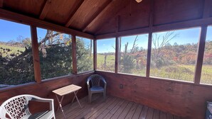 Una terraza de madera con una mesa y dos sillas, amplias ventanas que dan a un paisaje boscoso.