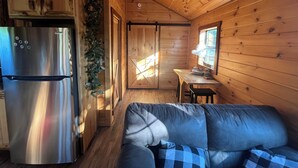 Un interior de cabaña acogedor, con un refrigerador de acero inoxidable, una mesa de comedor de madera y un sofá azul a cuadros.