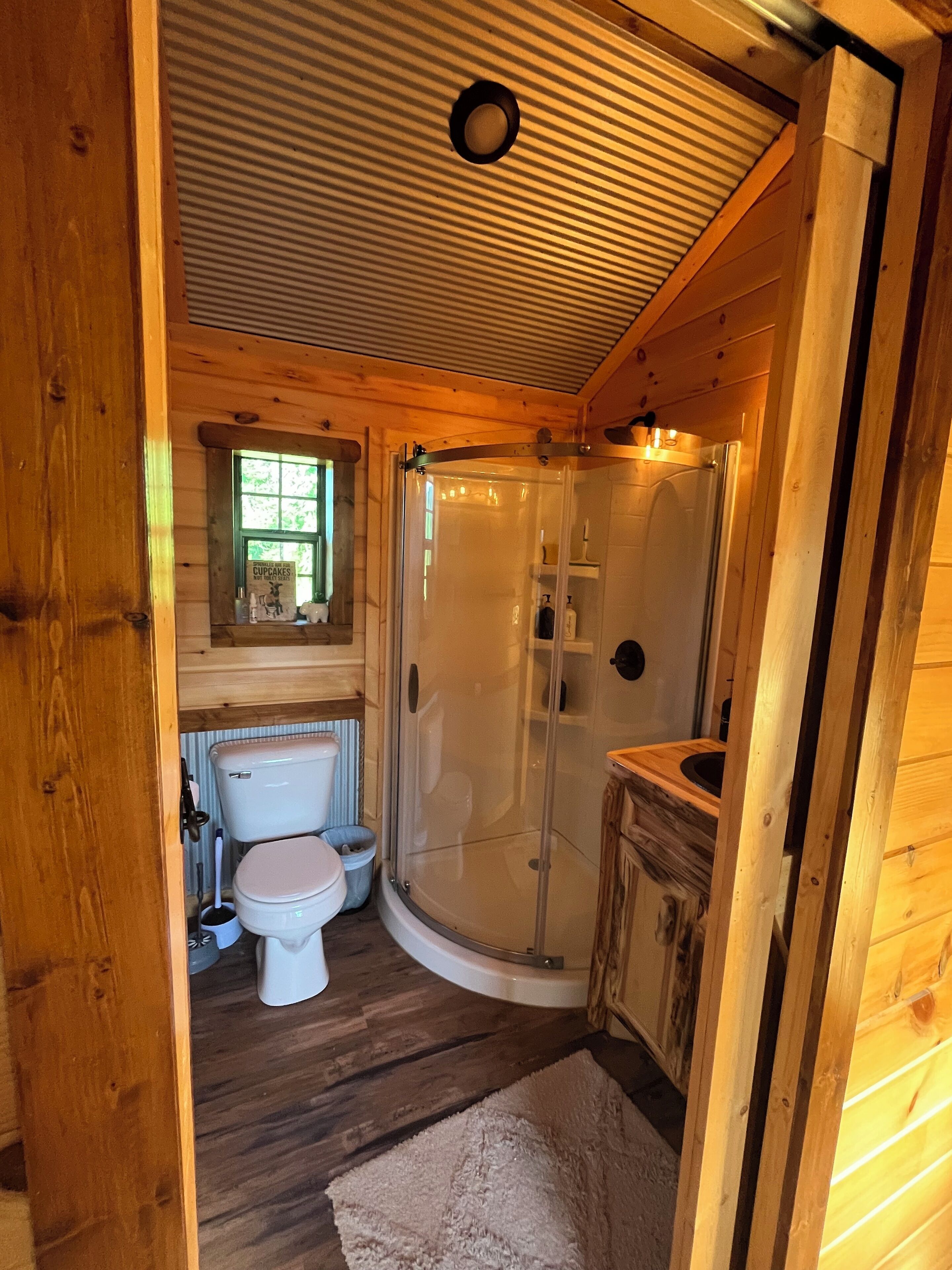 A wooden cabin bathroom with a toilet, sink, and shower.