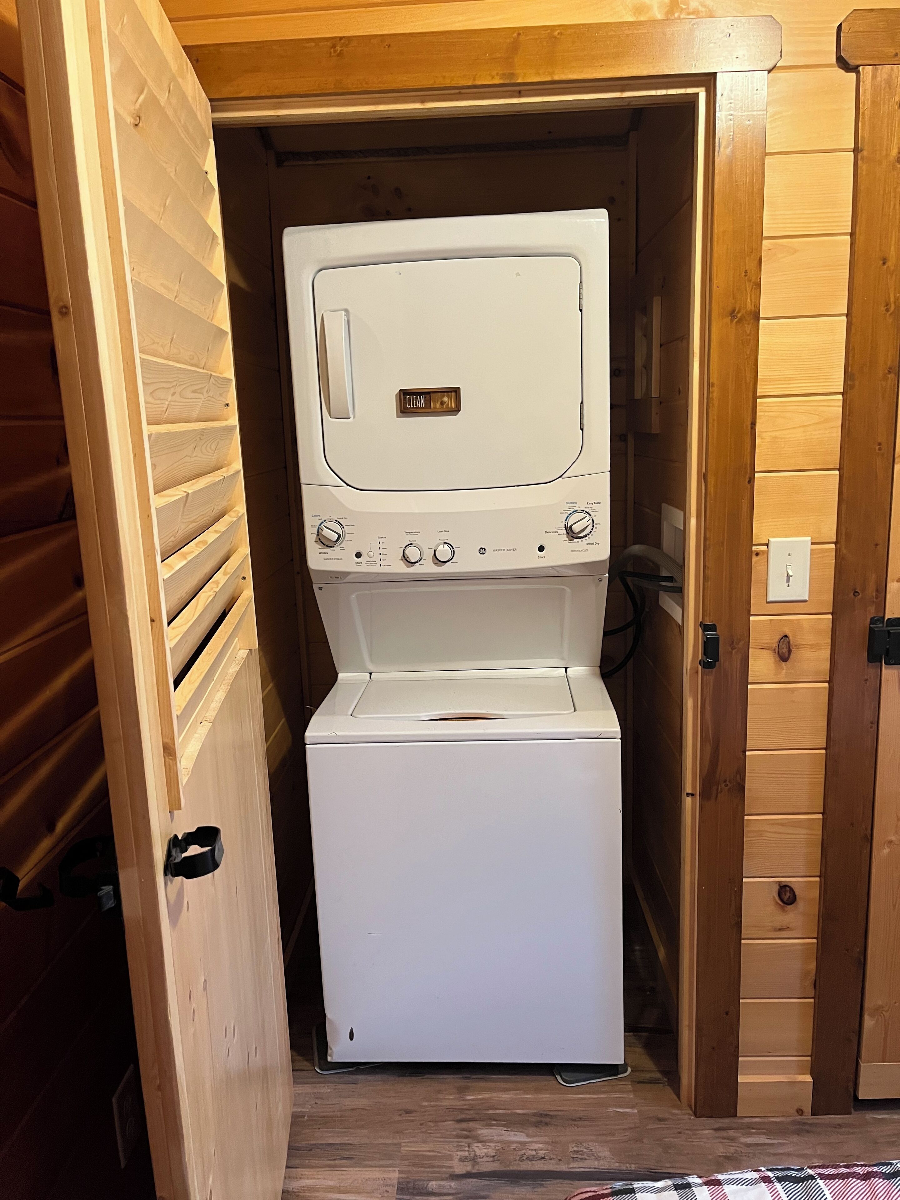 Ein kompaktes, weißes, an der Wand befestigtes Wasch- und Trocknergerät mit 'CLEAN'-Anzeige, in einem Holzschrank mit Tür untergebracht.