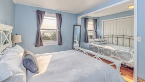 A bedroom with two beds, a window with curtains, a chandelier, and a white door. - 3-bedroom vacation home just 10 minutes from Adirondack Park (Ticonderoga)