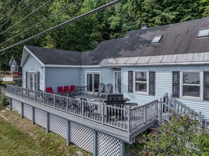 A two-story house with a covered patio area, a deck, and a small outdoor seating area with chairs.