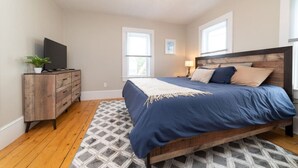 A bedroom with a wooden bed, a dresser, a TV, and a patterned rug.