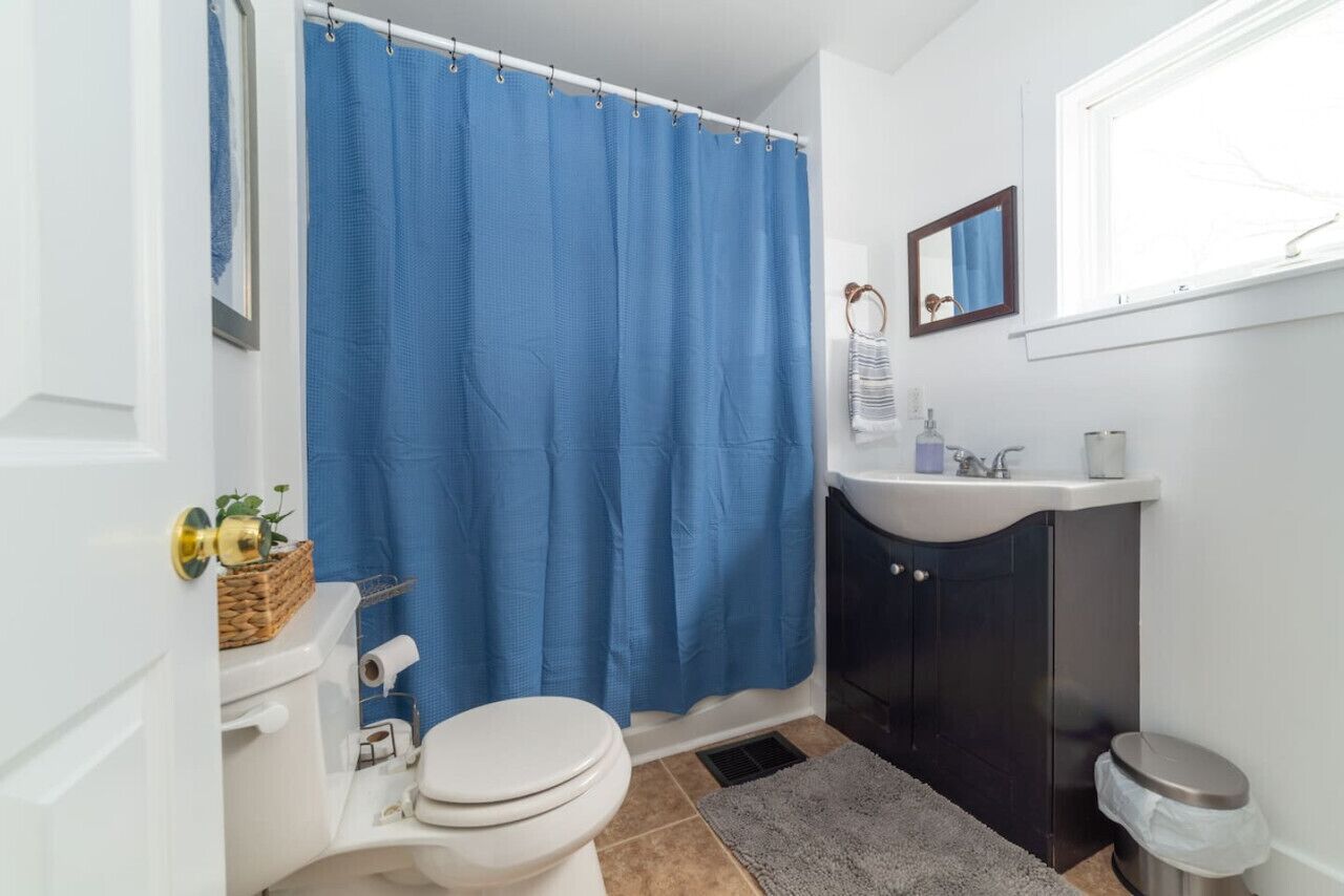 A bathroom with a white toilet, a blue shower curtain, a sink, and a mirror.