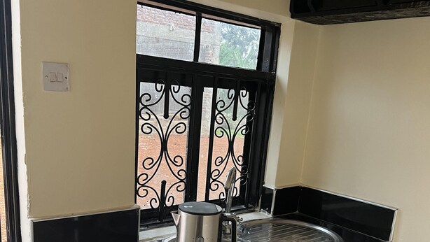 A compact kitchen with a black countertop, a stainless steel kettle, and a window with decorative black iron bars.