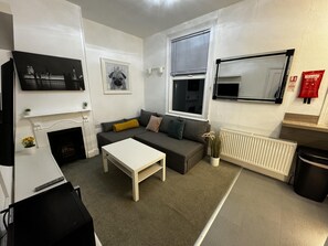 A modern living room with a fireplace, a sofa, a coffee table, a TV, and a radiator. - Onsite Apartments in Central Brentwood (Brentwood)