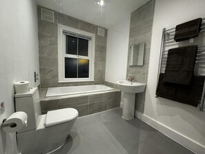 A modern bathroom with a toilet, bathtub, and sink. - Onsite Apartments in Central Brentwood (Brentwood)