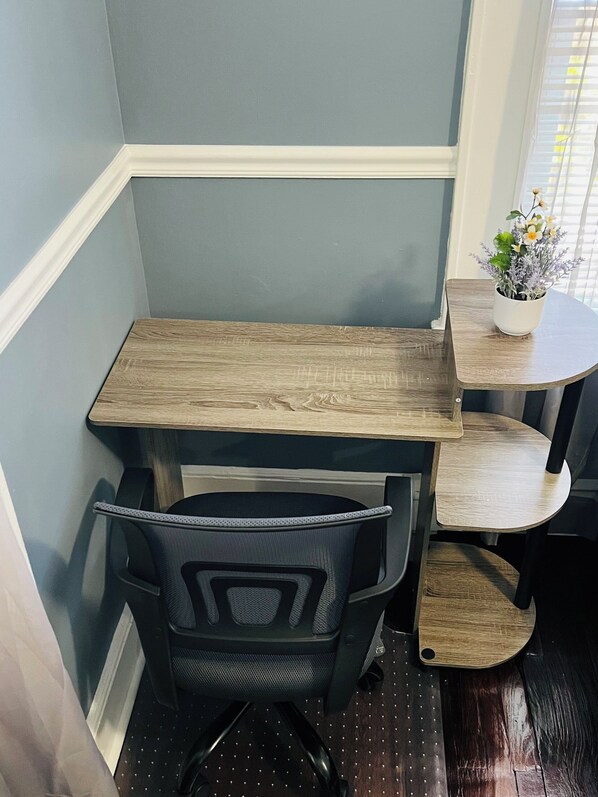 A corner desk with a chair, a small table with a potted plant, and a window with blinds.