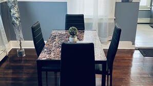 Uma sala de jantar com uma mesa de mármore, quatro cadeiras pretas, uma pequena planta em vaso e uma escultura à esquerda.