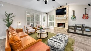 A living room with a leather sofa, a patterned ottoman, a round coffee table, a fireplace, and a TV mounted on the wall. - Y'all Stay Here Inn (Austin)