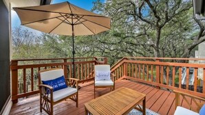 A wooden deck with outdoor furniture, including two chairs and a table, and a large umbrella providing shade. - Y'all Stay Here Inn (Austin)