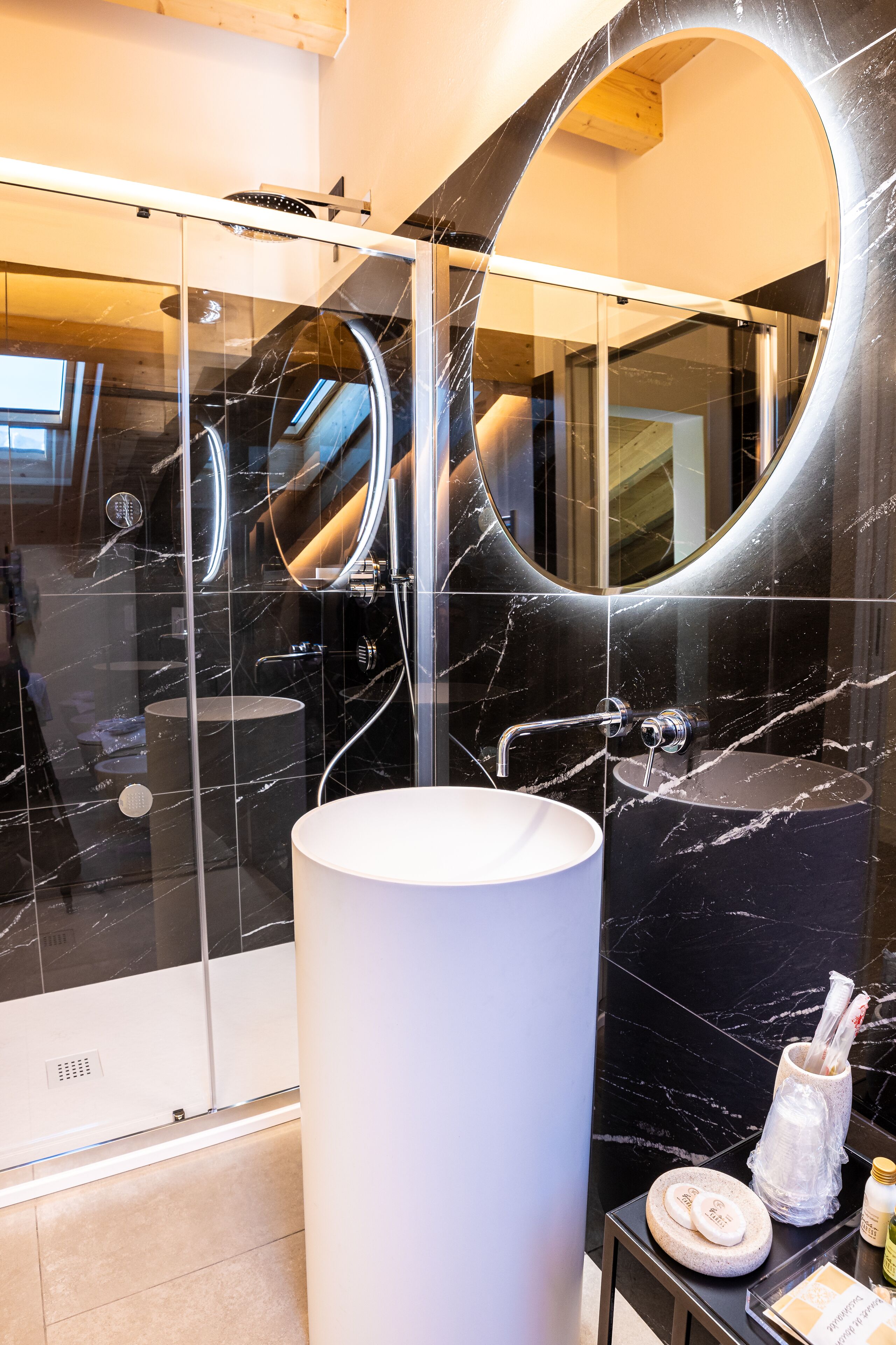 A modern bathroom with a glass-enclosed shower, a large white sink, and a marble-tiled wall.