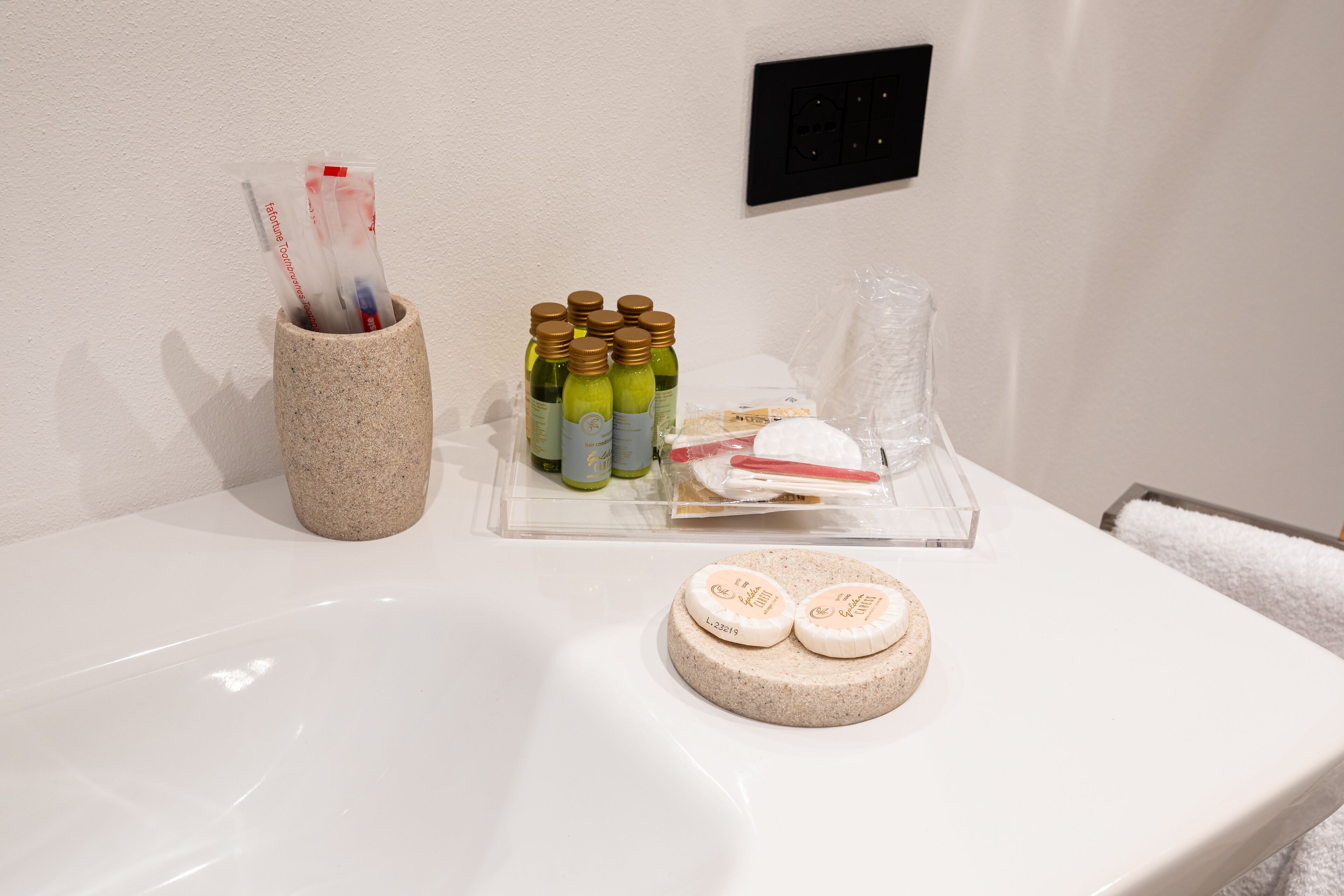 Un lavabo de baño con artículos de aseo, como botellas, jabón y un porta cepillos de dientes.