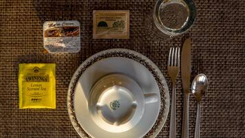 Una mesa dispuesta con un plato blanco, una copa, una cuchara, un tenedor, un cuchillo, un paquete de té Twinings Aroma de Limón, una caja de leche Major y un vaso de agua.