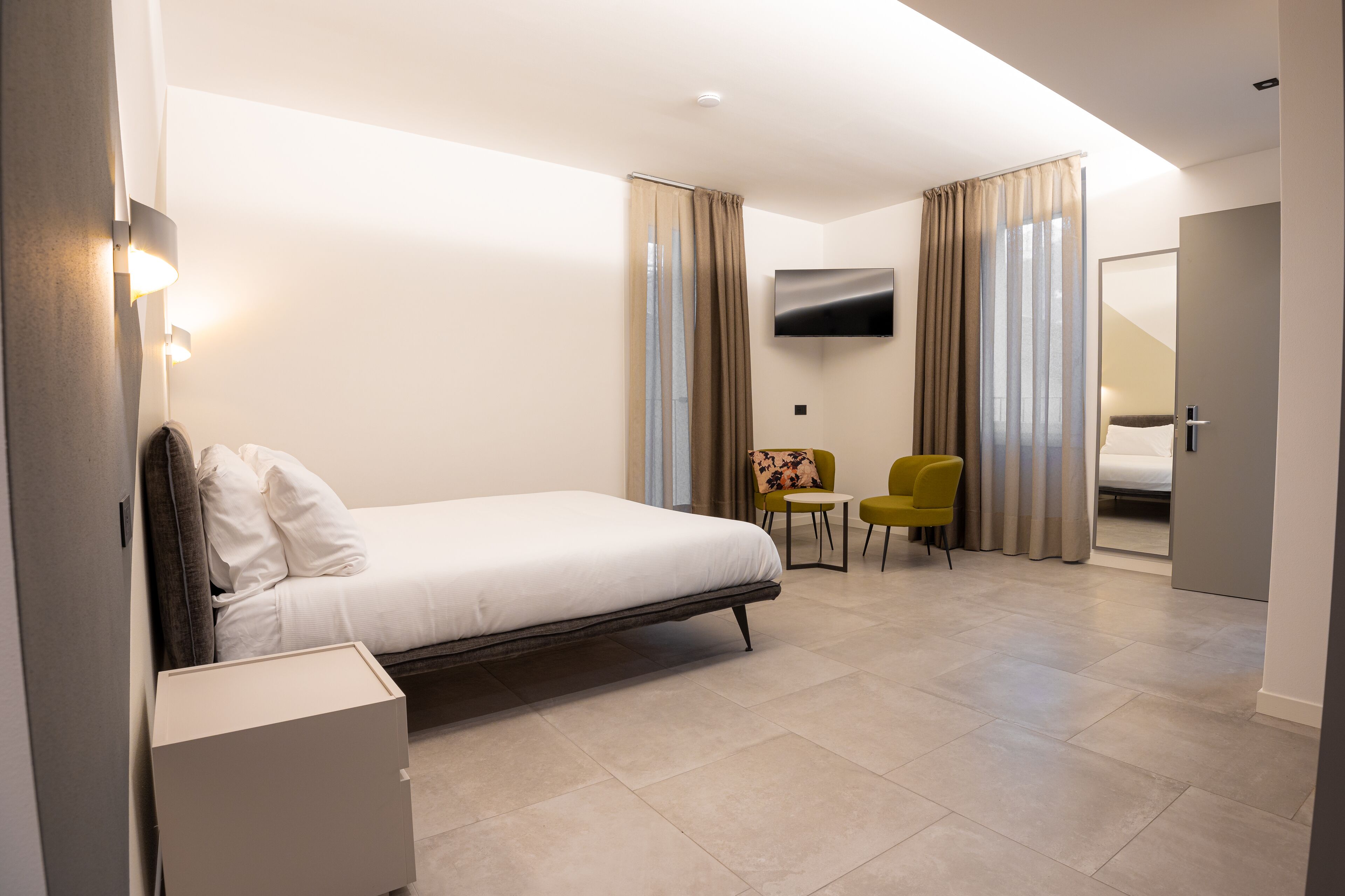 Une chambre d’hôtel moderne, équipée d’un lit, d’une petite table, d’une chaise et d’un téléviseur fixé au mur.