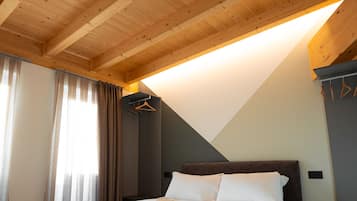 A bedroom with a wooden ceiling, a bed with white bedding, a dark headboard, and a hanging coat rack.