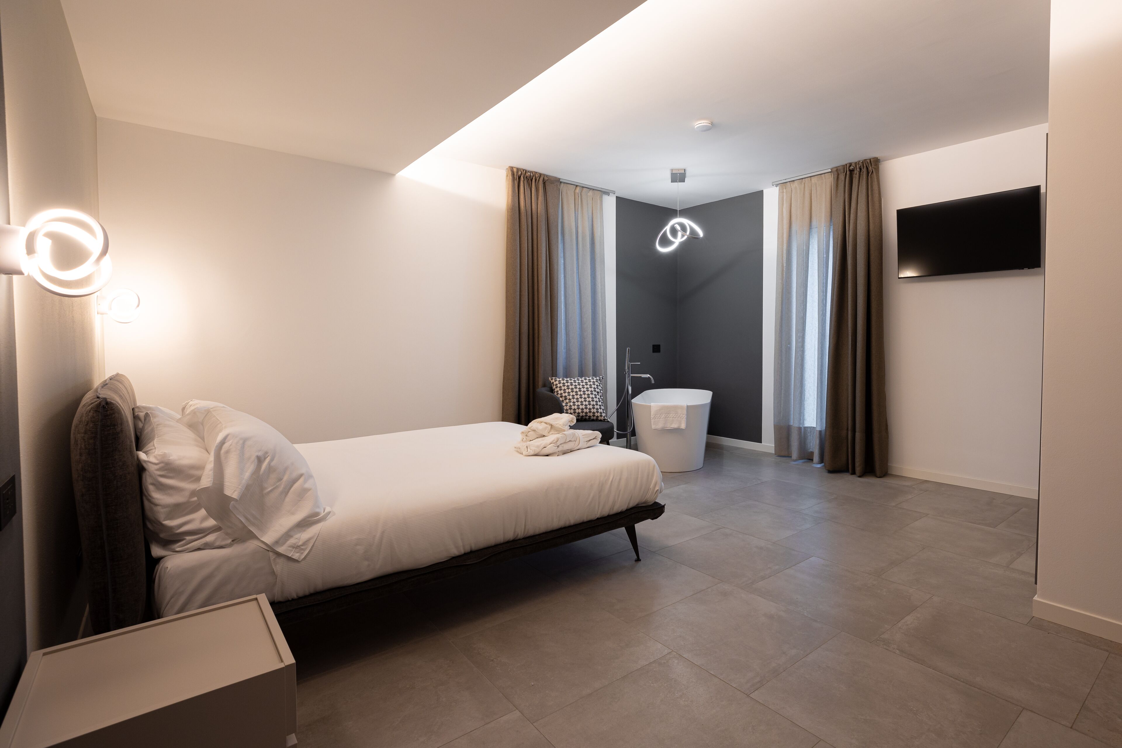 Habitació d'hotel moderna amb llit, una taula de nit, televisió de pantalla plana penjada a la paret i bany amb vàter i dutxa.