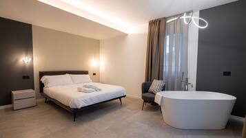 Ein modernes Schlafzimmer mit Bett, Nachttischen, einem Sessel, einer Badewanne und einer Deckenleuchte.