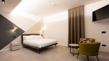 Una habitación de hotel moderna con una cama, una mesita pequeña, un sillón verde y un televisor de pantalla plana montado en la pared.