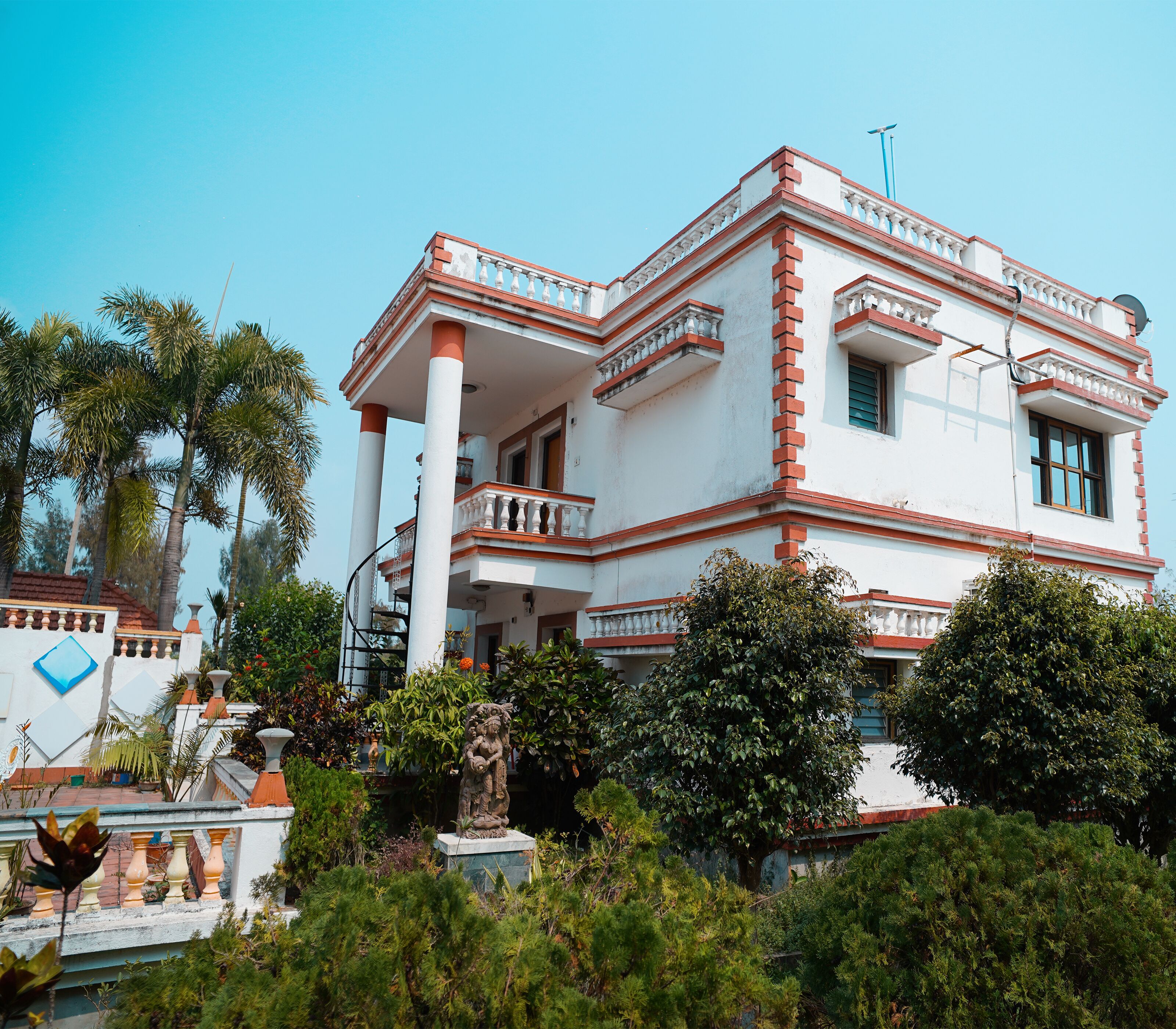 Un edificio grande de varios pisos con fachada blanca y detalles en rojo, que presenta balcones y una estatua en primer plano.