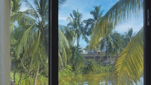 A view through a window of a tropical landscape with palm trees and a body of water. - Icon Heritage Bakkhali - Where the Sea Meets Luxury (Kakdwip)
