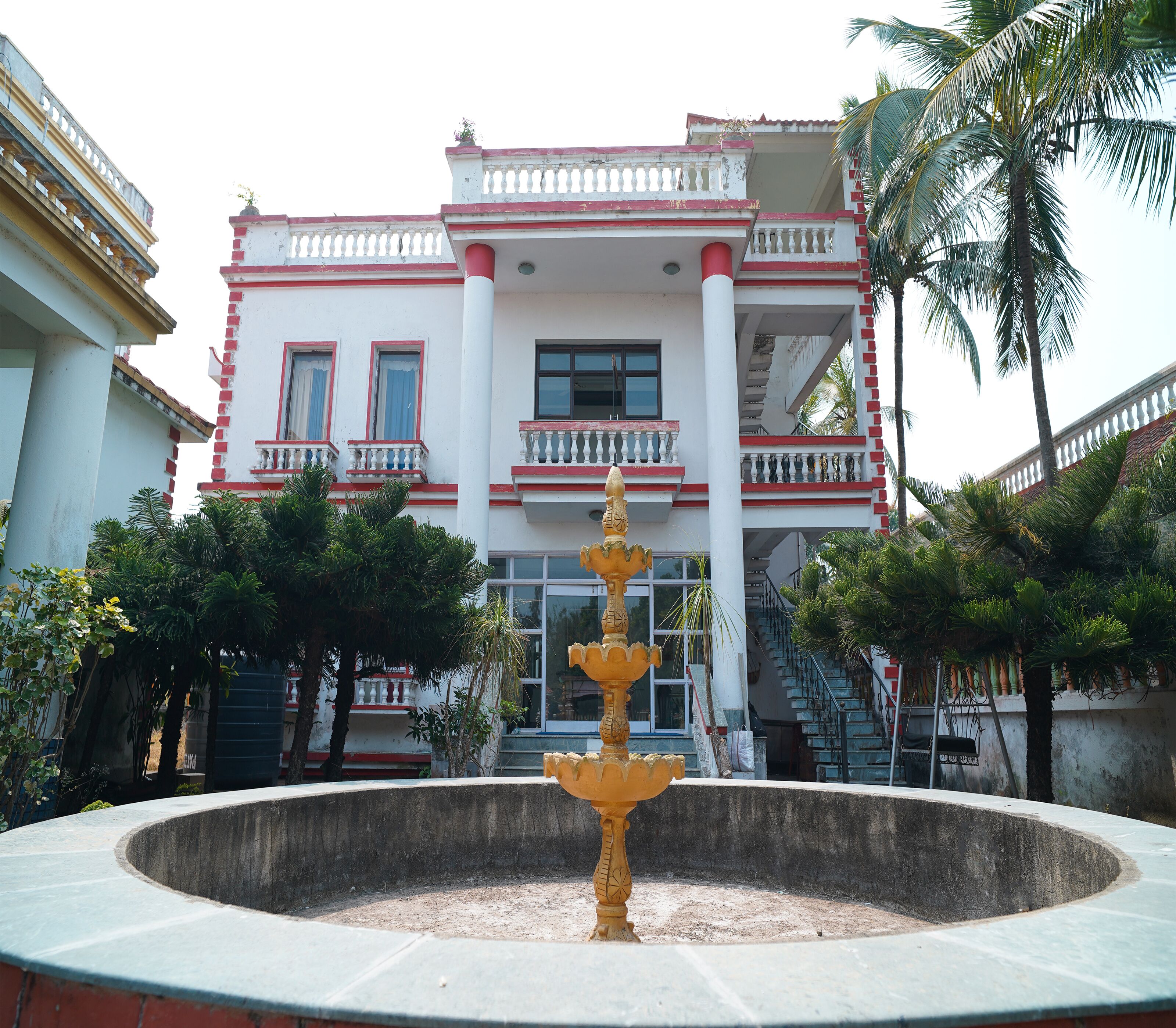 A building with a white facade and red accents, a central fountain, and surrounding greenery.