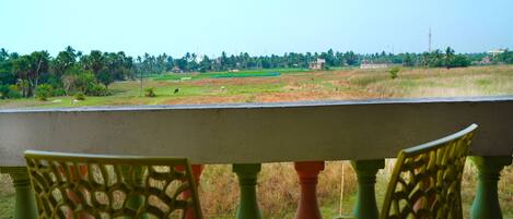A balcony with a view of a rural landscape, including fields and trees.