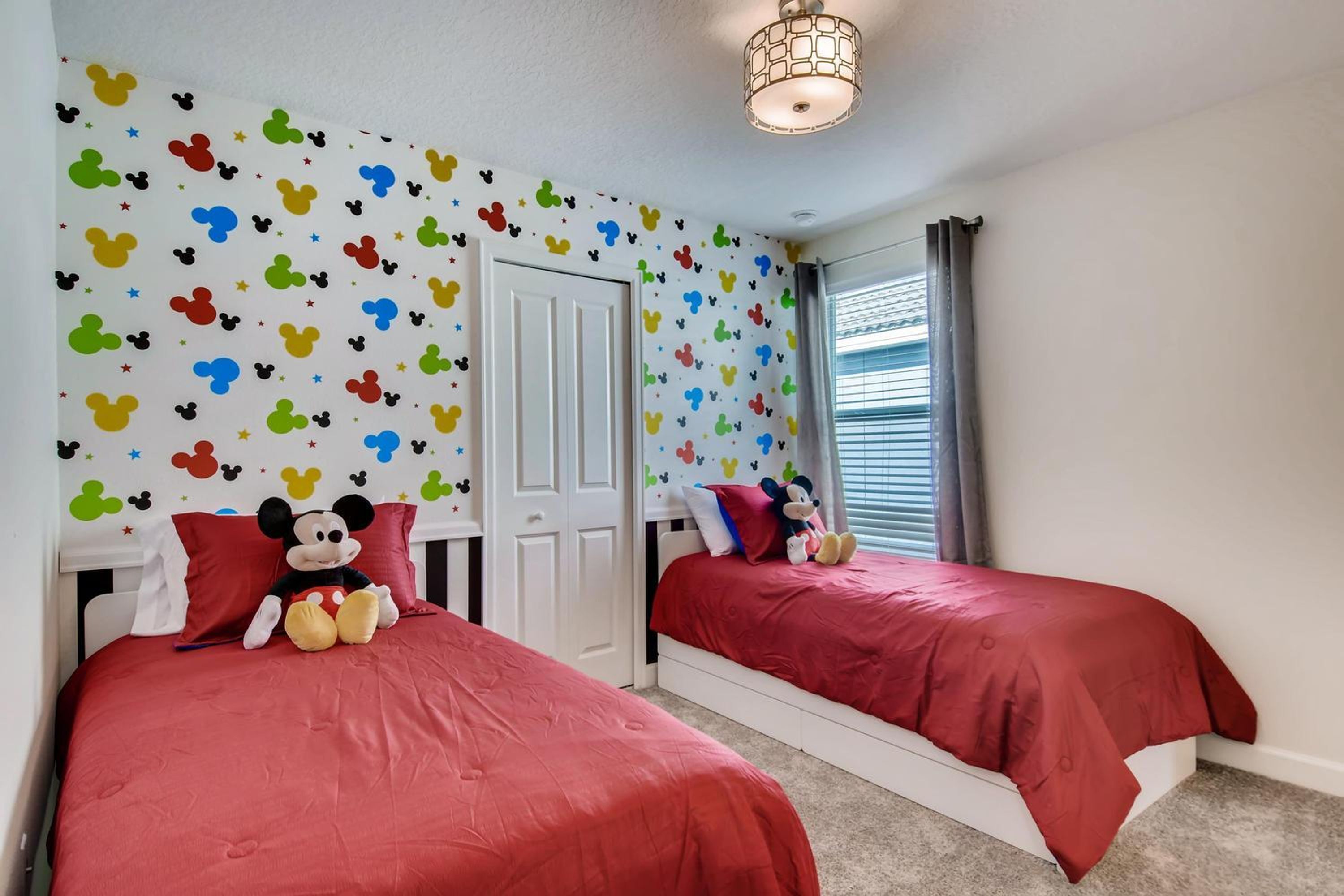 A bedroom with two beds, each with red bedding and Mickey Mouse-themed wall decals.