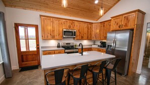 A modern kitchen with wooden cabinets, a stainless steel refrigerator, a microwave, and a large island with bar stools.