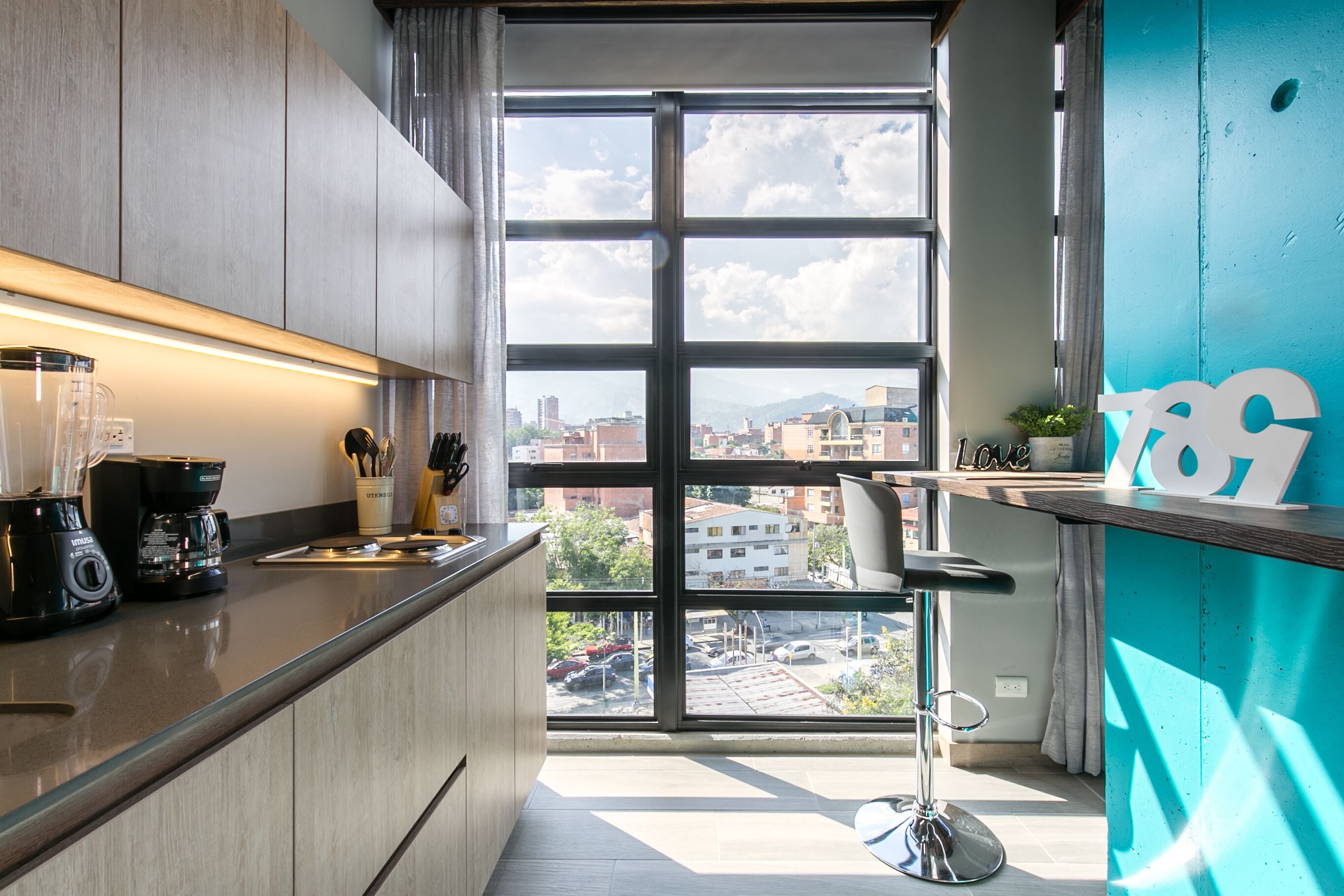 Una cocina moderna con un ventanal grande, una cafetera y un taburete de bar.