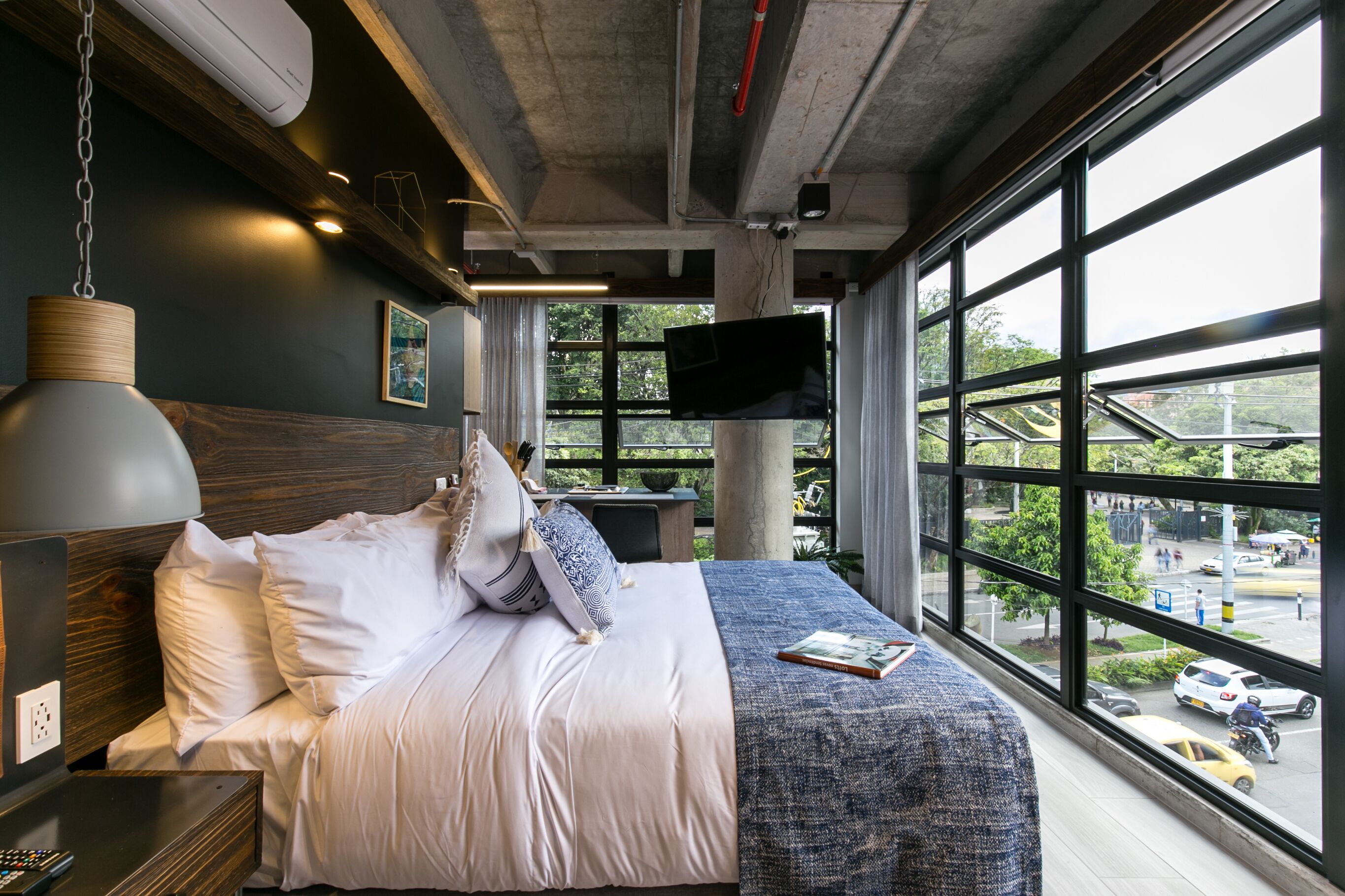 Une chambre d’hôtel moderne dotée d’un grand lit, d’un téléviseur à écran plat fixé au mur et offrant une vue sur la ville grâce à de grandes fenêtres.