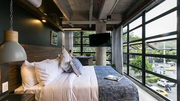 Une chambre d’hôtel moderne dotée d’un grand lit, d’un téléviseur à écran plat fixé au mur et offrant une vue sur la ville grâce à de grandes fenêtres.