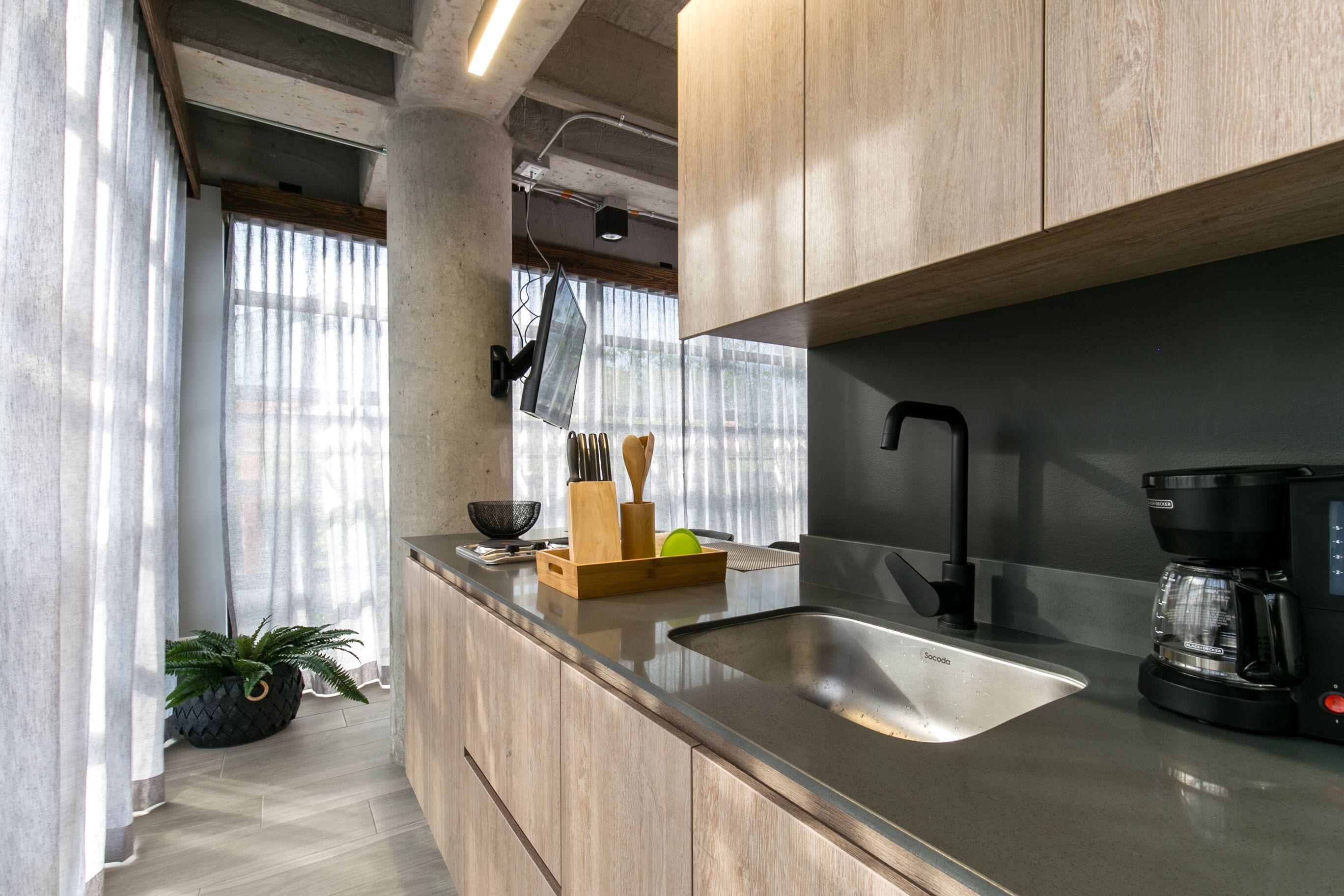 A modern kitchen with a stainless steel sink, wooden cabinets, and a coffee maker.