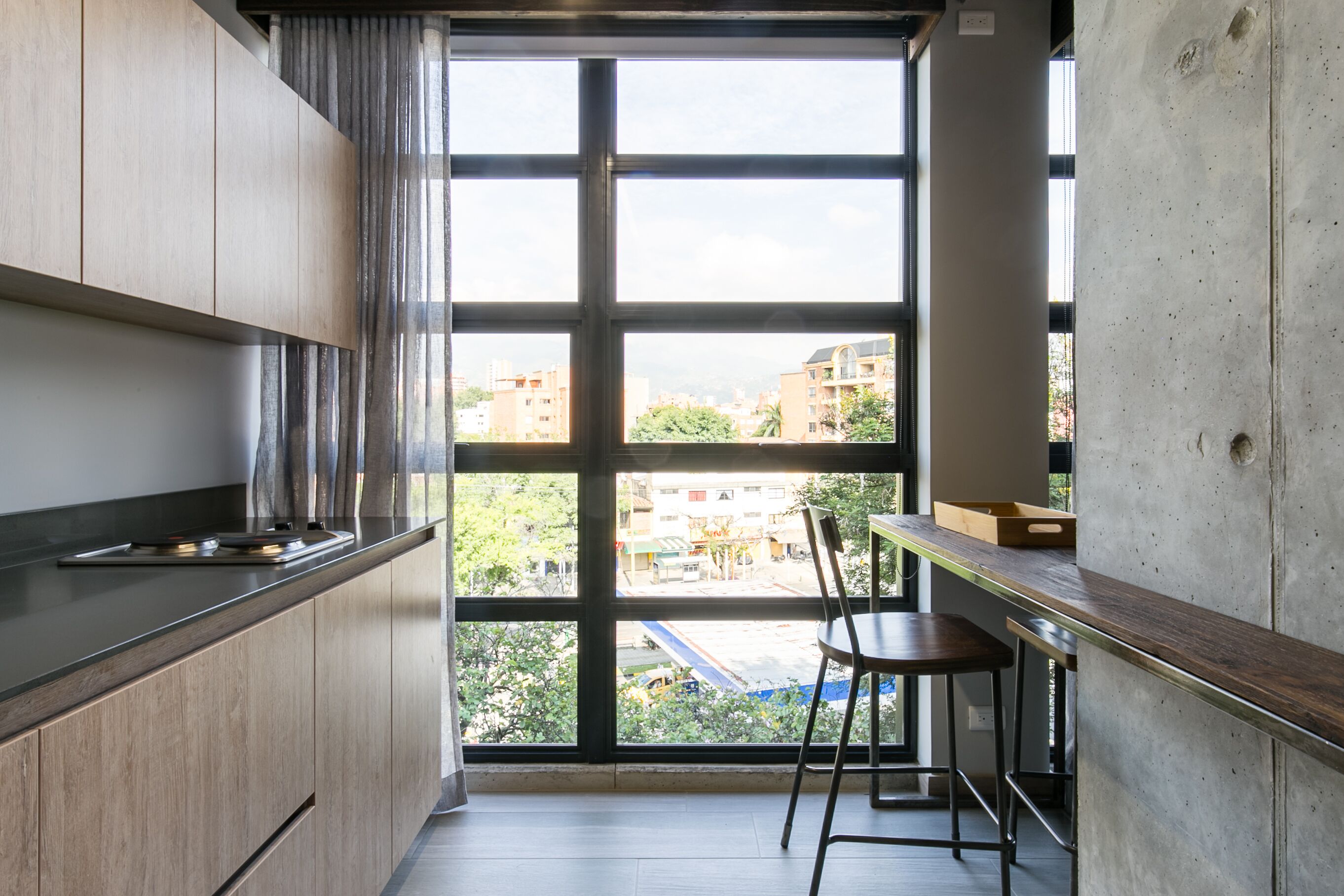 A modern kitchen with a large window, a wooden countertop, and a dining area with a chair.