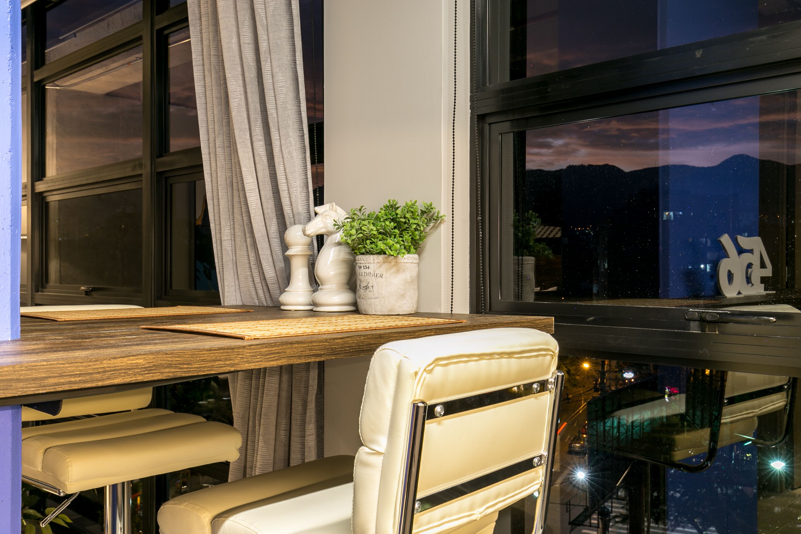 A modern room with a wooden desk, a white chair, a potted plant, and a view of the mountains through the window.